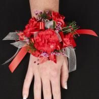 Red floral corsage with silver ribbon on a hand against a black background