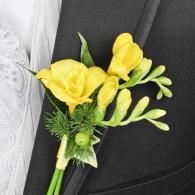 Yellow boutonniere with roses and greenery pinned to a black suit lapel