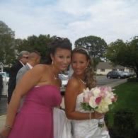 Two women posing outdoors, one in a pink dress and one holding a bouquet in a white dress.