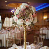 Tall floral centerpiece with pale pink and white roses at a decorated banquet table in a warm ballroom