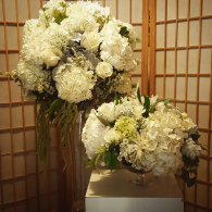 White floral arrangements on a pedestal in front of a wooden shoji screen
