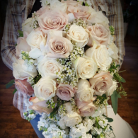 Large bouquet of pale roses, cream flowers, and greenery held in someone’s hands