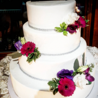Three-tier white wedding cake with silver trim and purple, pink, and white flowers