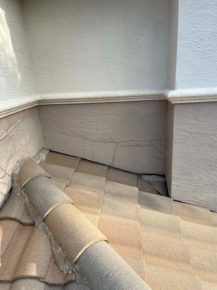 A close up of a tiled roof with a white wall in the background.