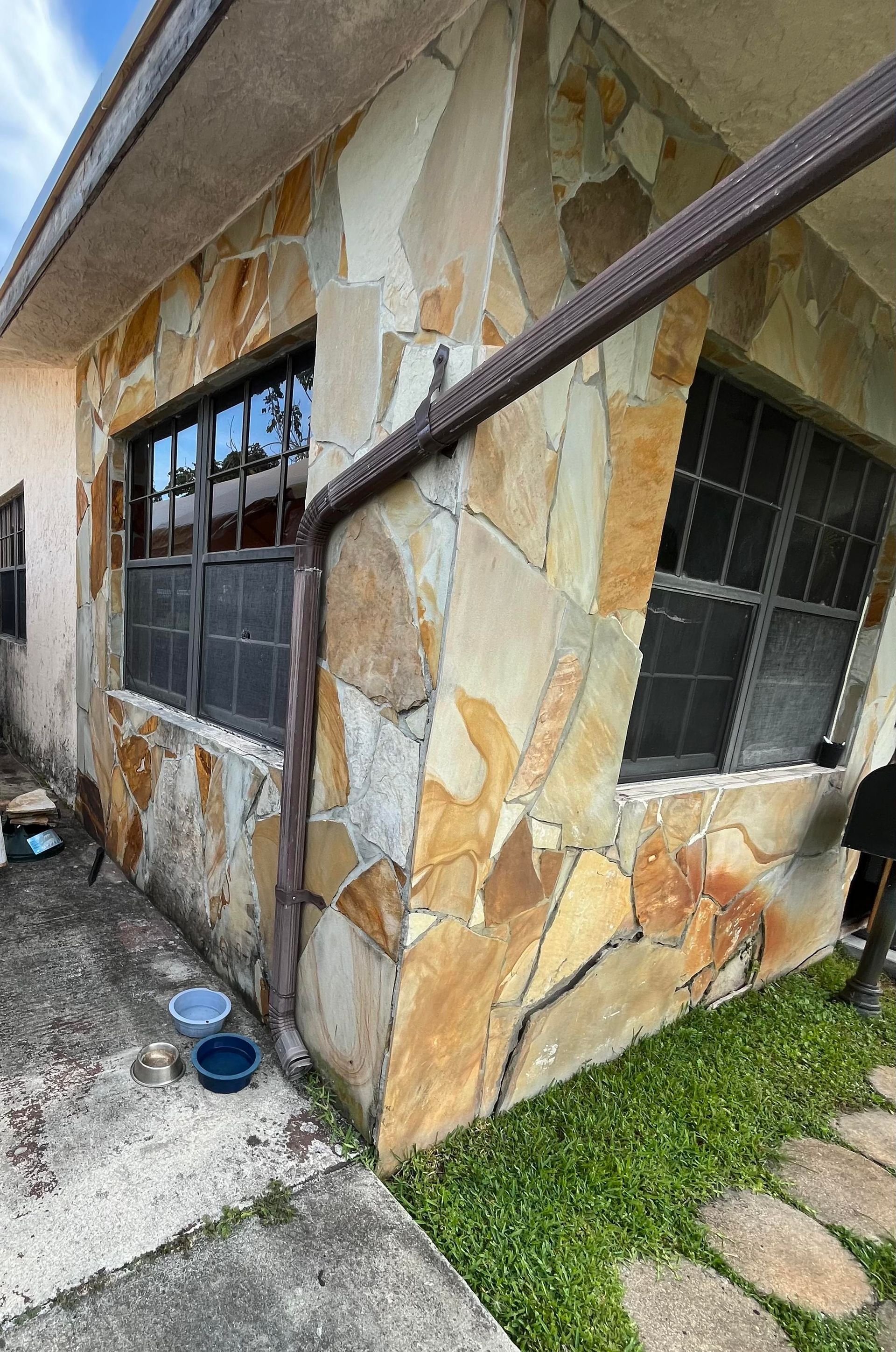 A house with a stone wall and a gutter on the side of it.