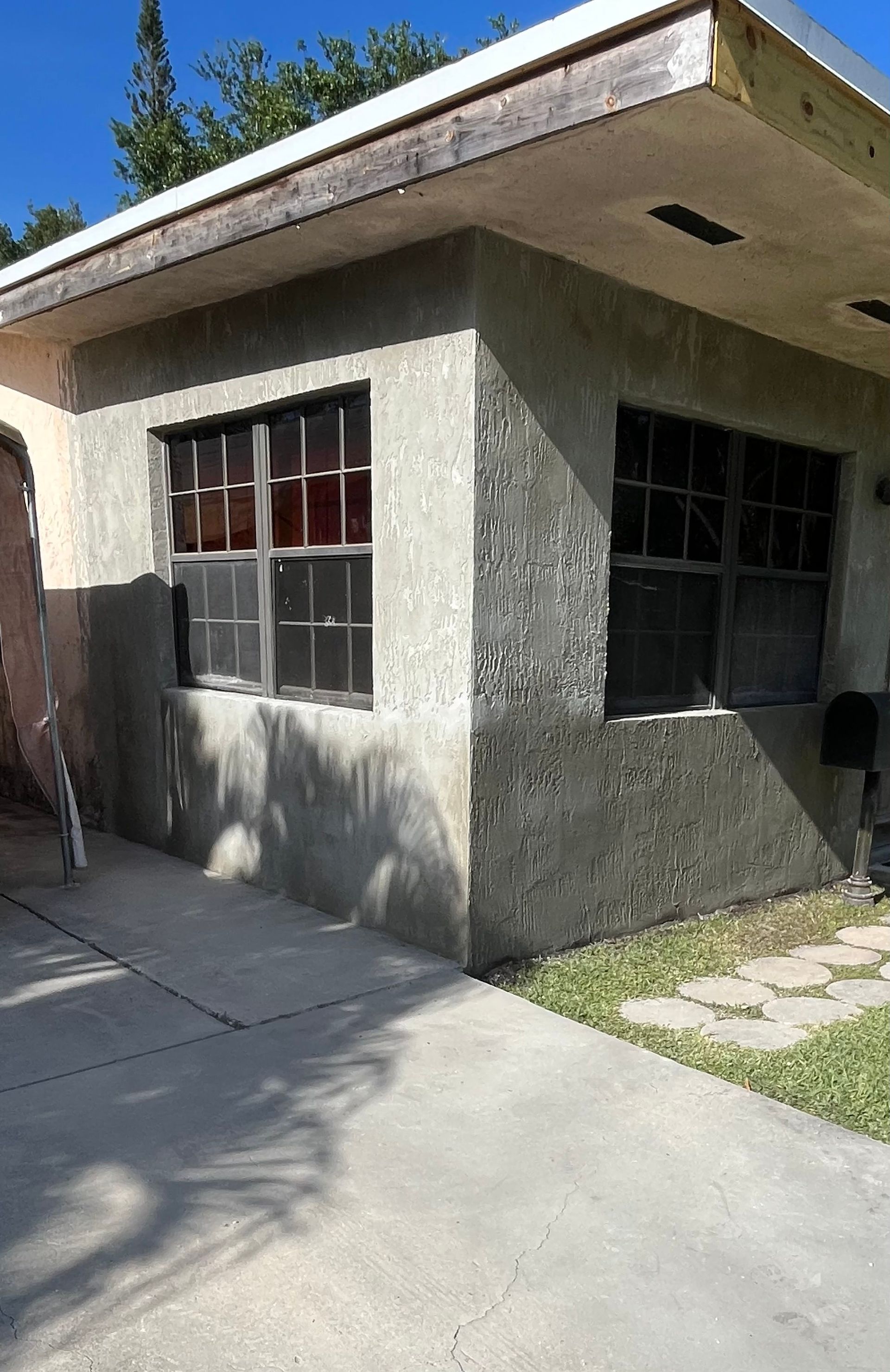 A small house with a lot of windows and a concrete driveway.
