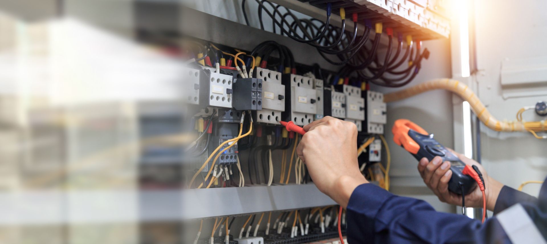 Ein Elektriker überprüft mit einem Multimeter die elektrische Verkabelung in einem industriellen Schaltschrank.