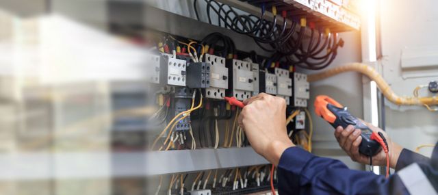 Ein Elektriker überprüft mit einem Multimeter die elektrische Verkabelung in einem industriellen Schaltschrank.