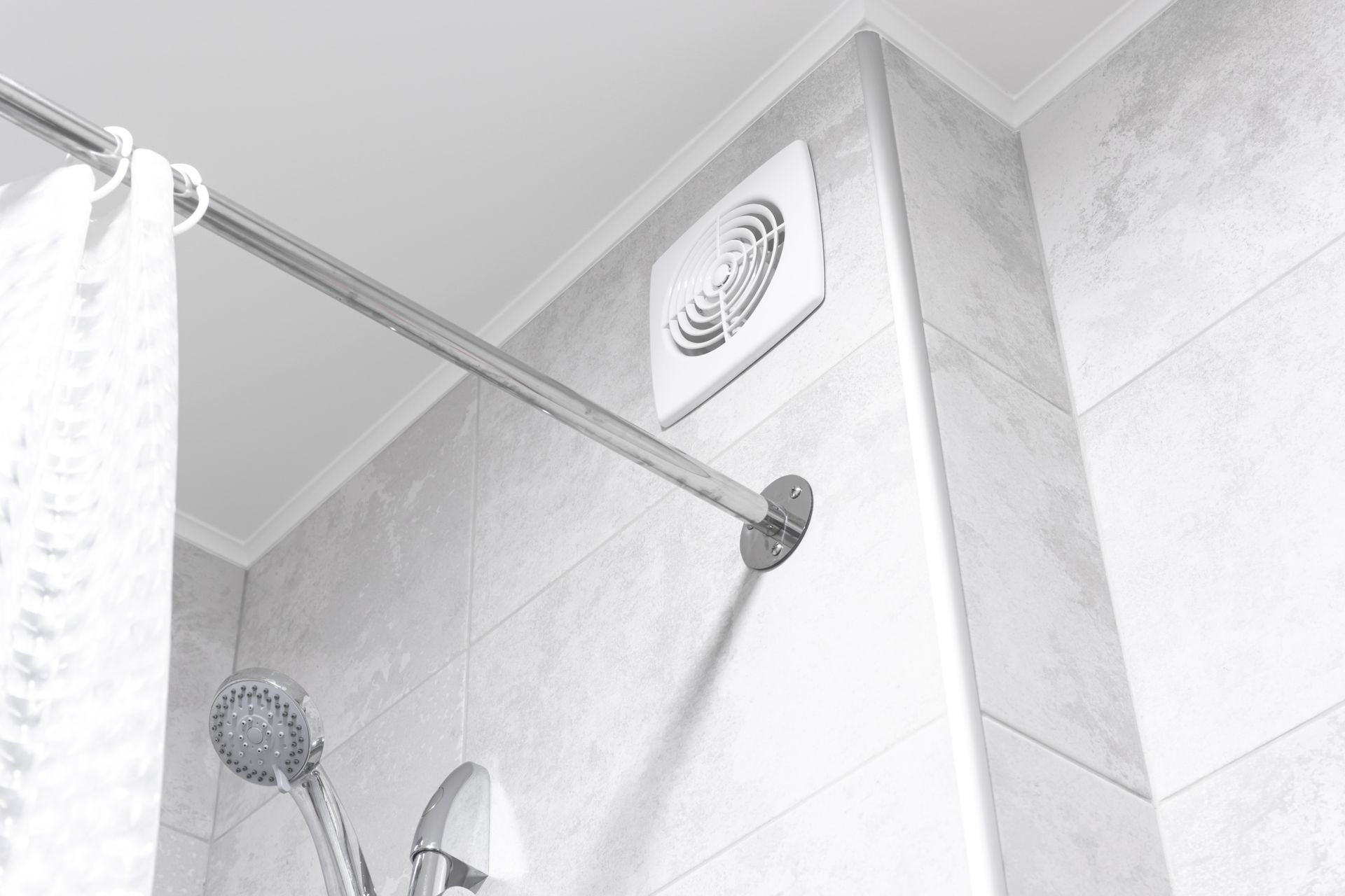 Dusche mit gefliesten Wänden, Duschkopf und Wandlüfter. Eine Duschvorhangstange ist sichtbar.