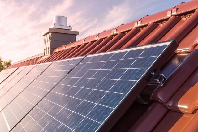 Solarpaneele auf einem roten Ziegeldach, im Hintergrund ein Schornstein.