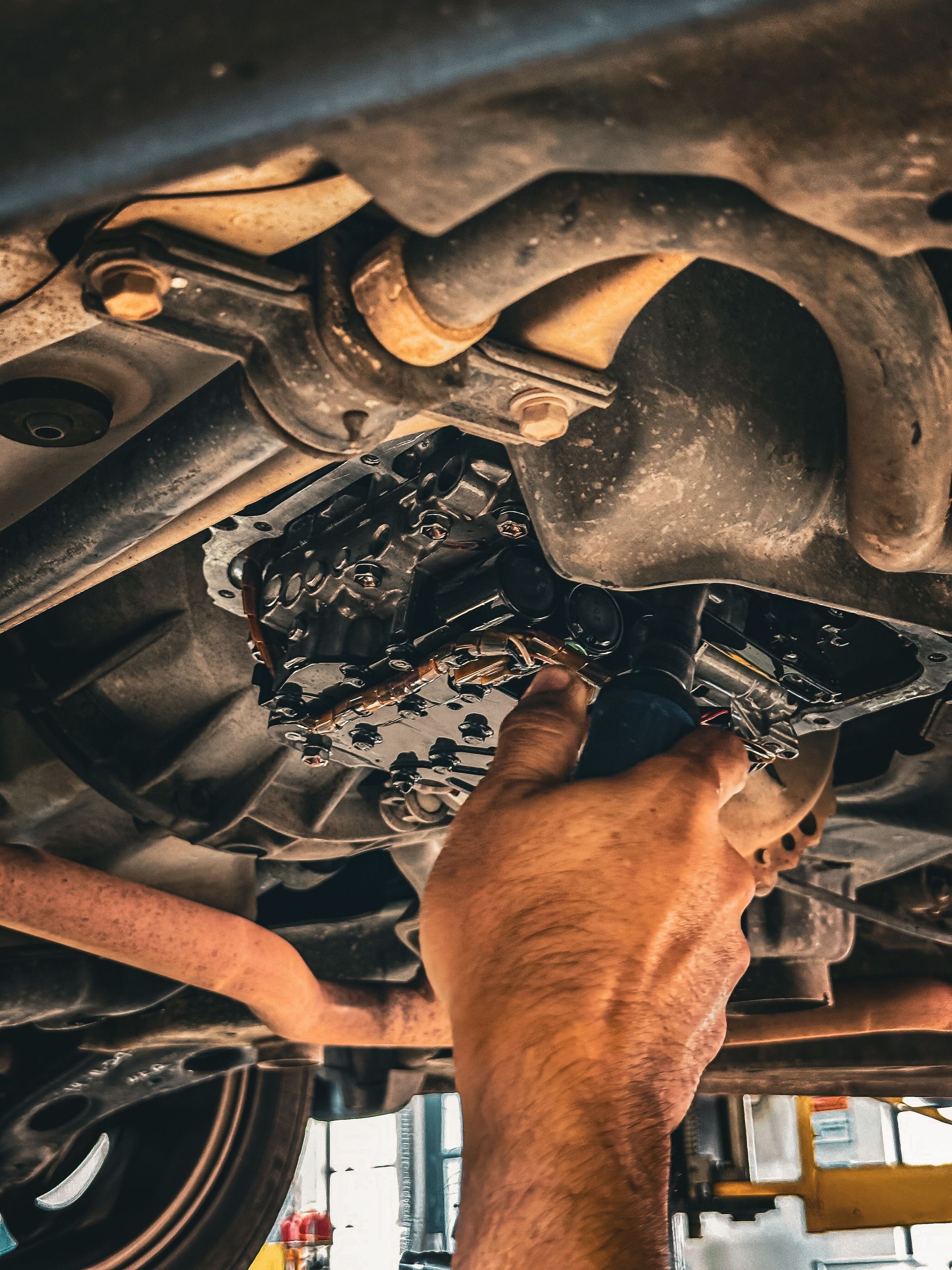 Mechanic working under a car, cleaning or repairing the engine with a tool. | Sulphur Automotive