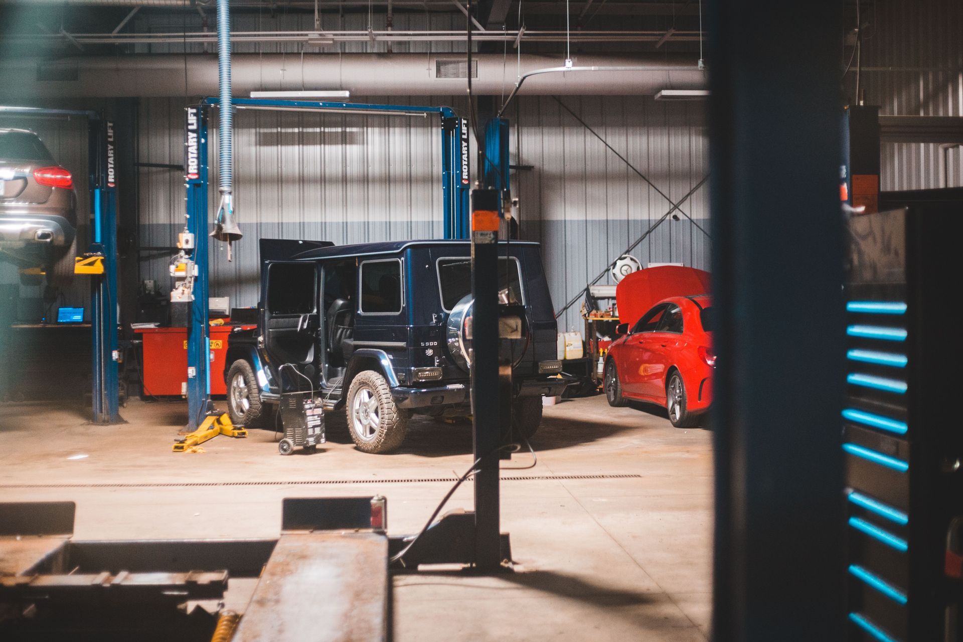 Auto shop garage with a black SUV on a lift, red car in back, and a worker near the vehicle | Sulphur Automotive