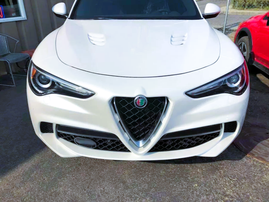 Front view of a white Alfa Romeo sports car parked outdoors, with a red car beside it.