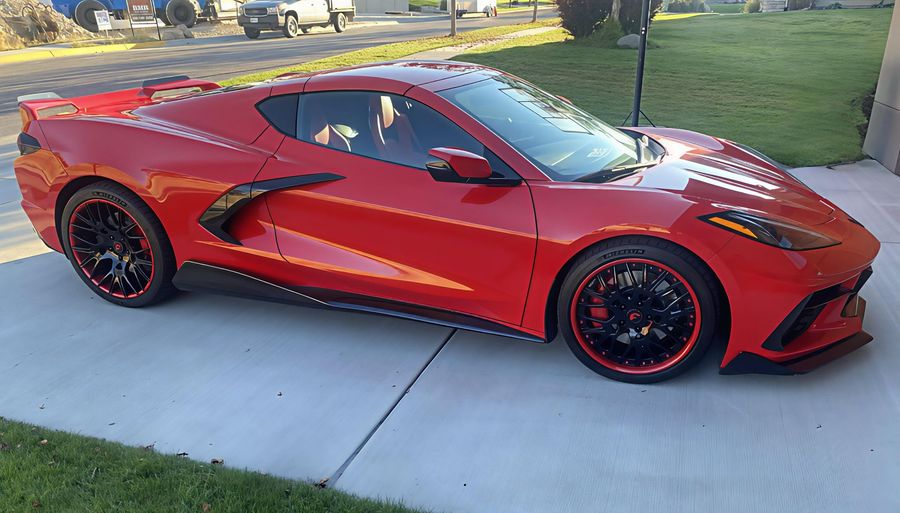 Red sports car with black rims parked on a driveway in a suburban yard.