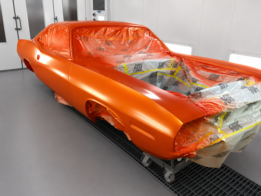 Orange classic car body wrapped in plastic in a workshop, under restoration