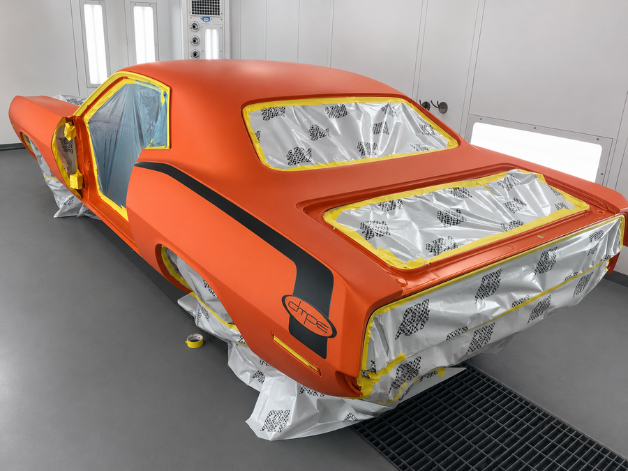 Orange sports car in a paint booth, covered with masking tape and paper for repainting