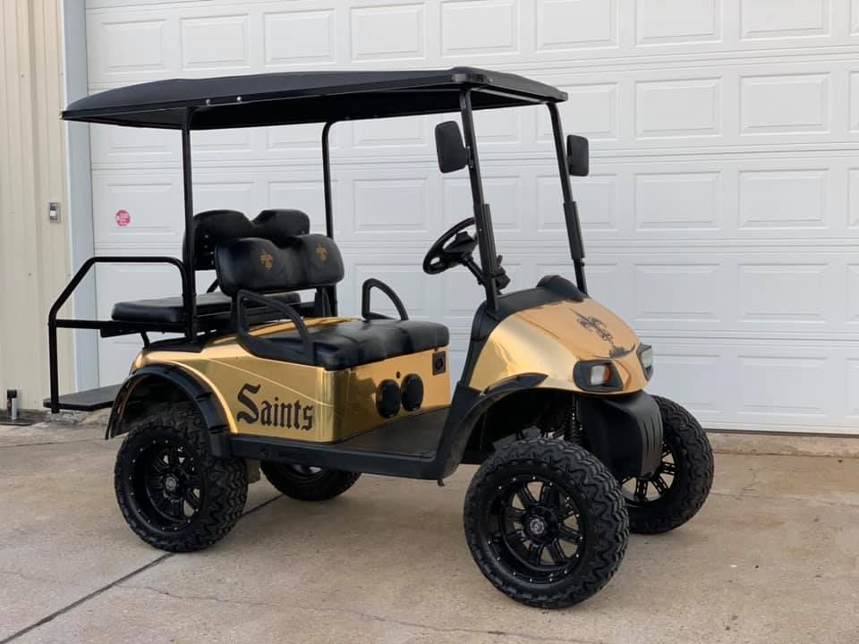 Tan and black custom golf cart with canopy and Saints logo parked on driveway