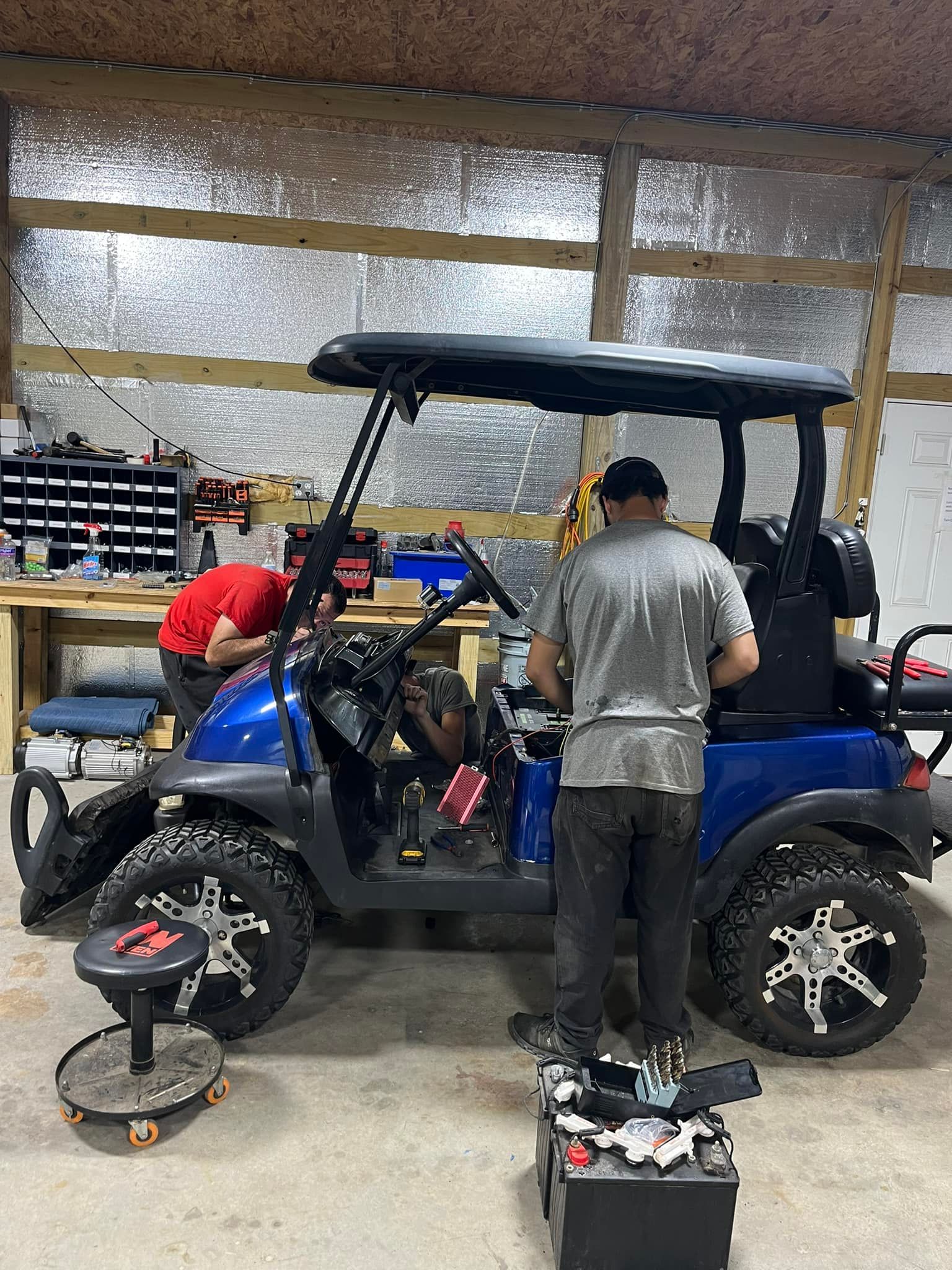 Blue off-road golf cart in a workshop with two people working on it and tools nearby