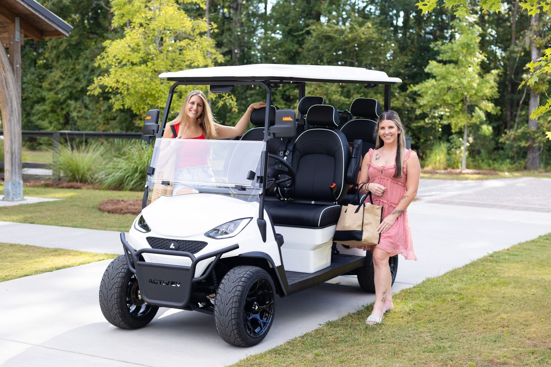 Two people beside a white golf cart on a driveway, with trees and grass in the background
