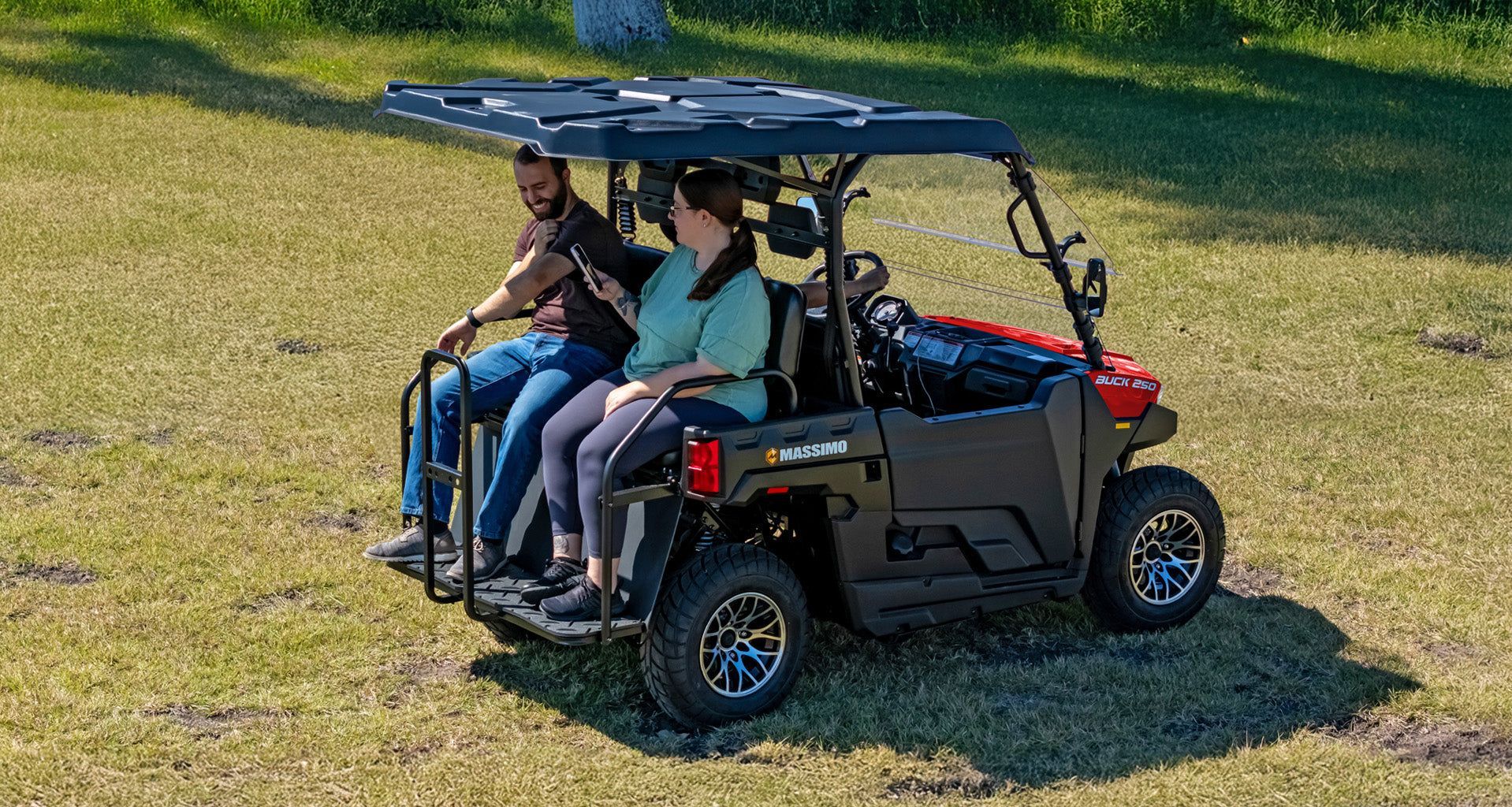Four people riding in a black golf cart on a grassy field under a canopy