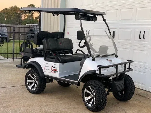White and black golf cart with roof, windshield, and off-road tires parked in front of a garage