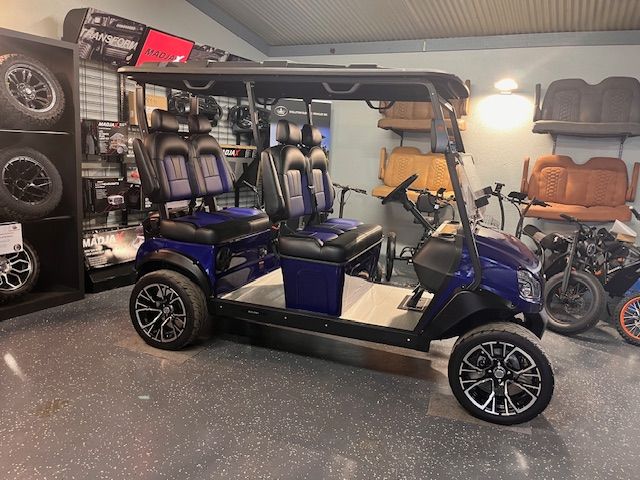 Blue golf cart with tan roof and seats displayed in a showroom, beside other vehicles.