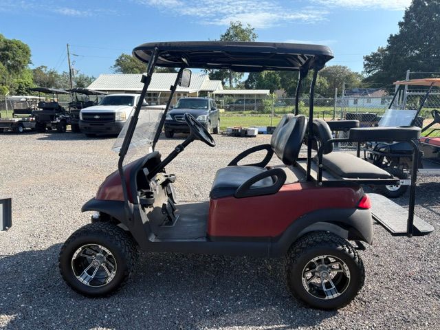 Beige golf cart parked on gravel in front of a white wall with logos.