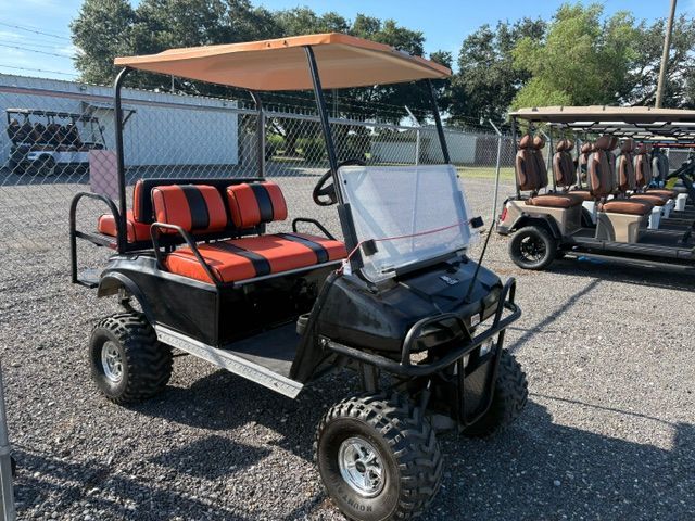 Beige golf cart parked on gravel in front of a white wall with logos.