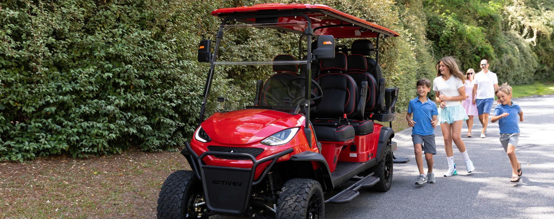 Red utility cart on a path with four people walking beside it near bushes
