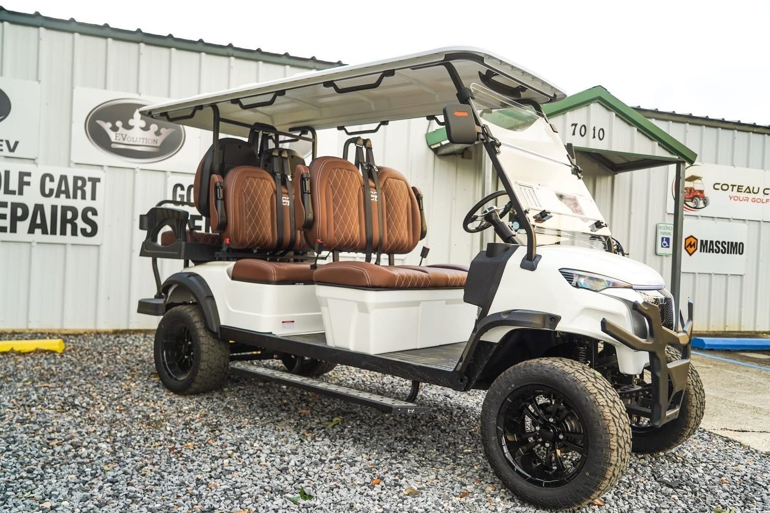 White golf cart with tan seats parked outside a repair shop on gravel