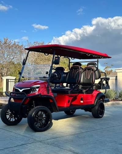 Red four-seat golf cart with roof parked on a driveway under a blue sky.