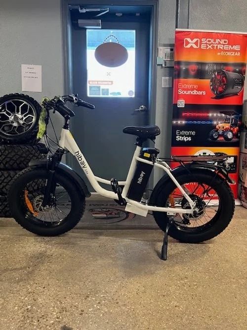 White electric bike displayed indoors beside a red bicycle shop sign.