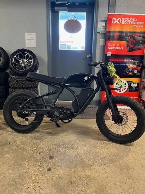 Black electric-style bike indoors beside stacked tires and a red display stand.