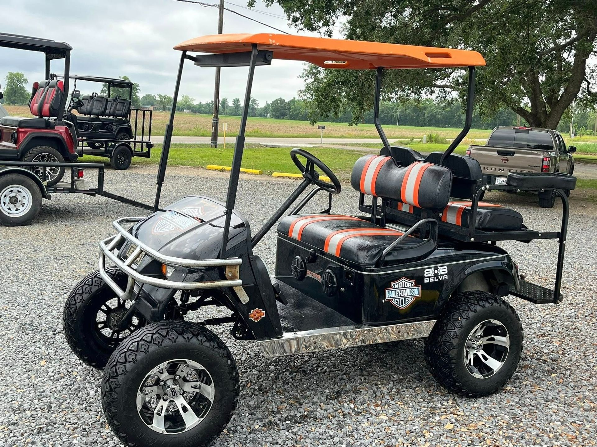 Black and orange lifted golf cart with orange canopy parked on gravel lot