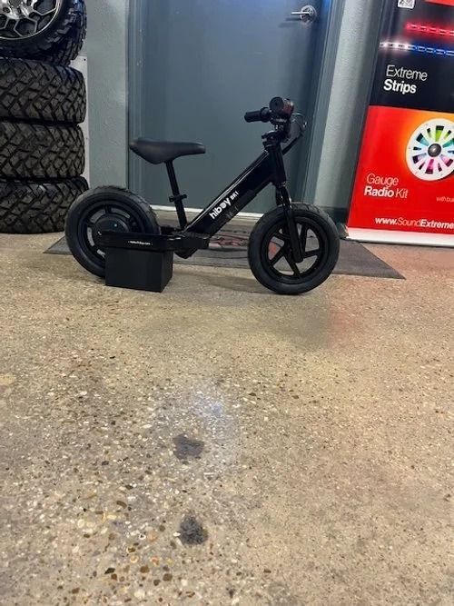 Black electric bicycle in a store entrance, with a rear child seat and a front basket on the floor.