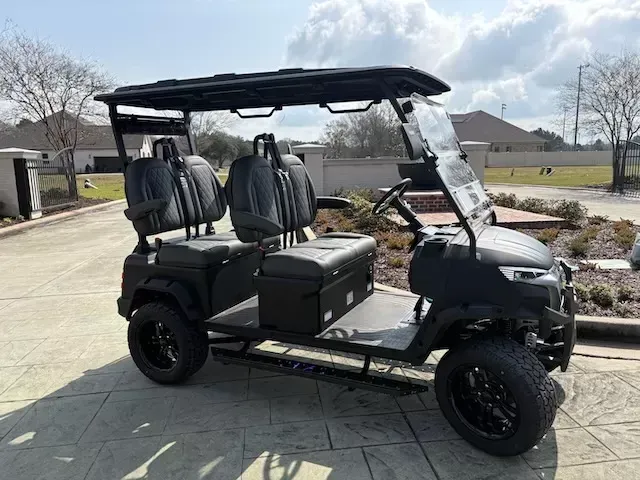 Black golf cart with roof and four seats parked on a driveway in a suburban neighborhood.