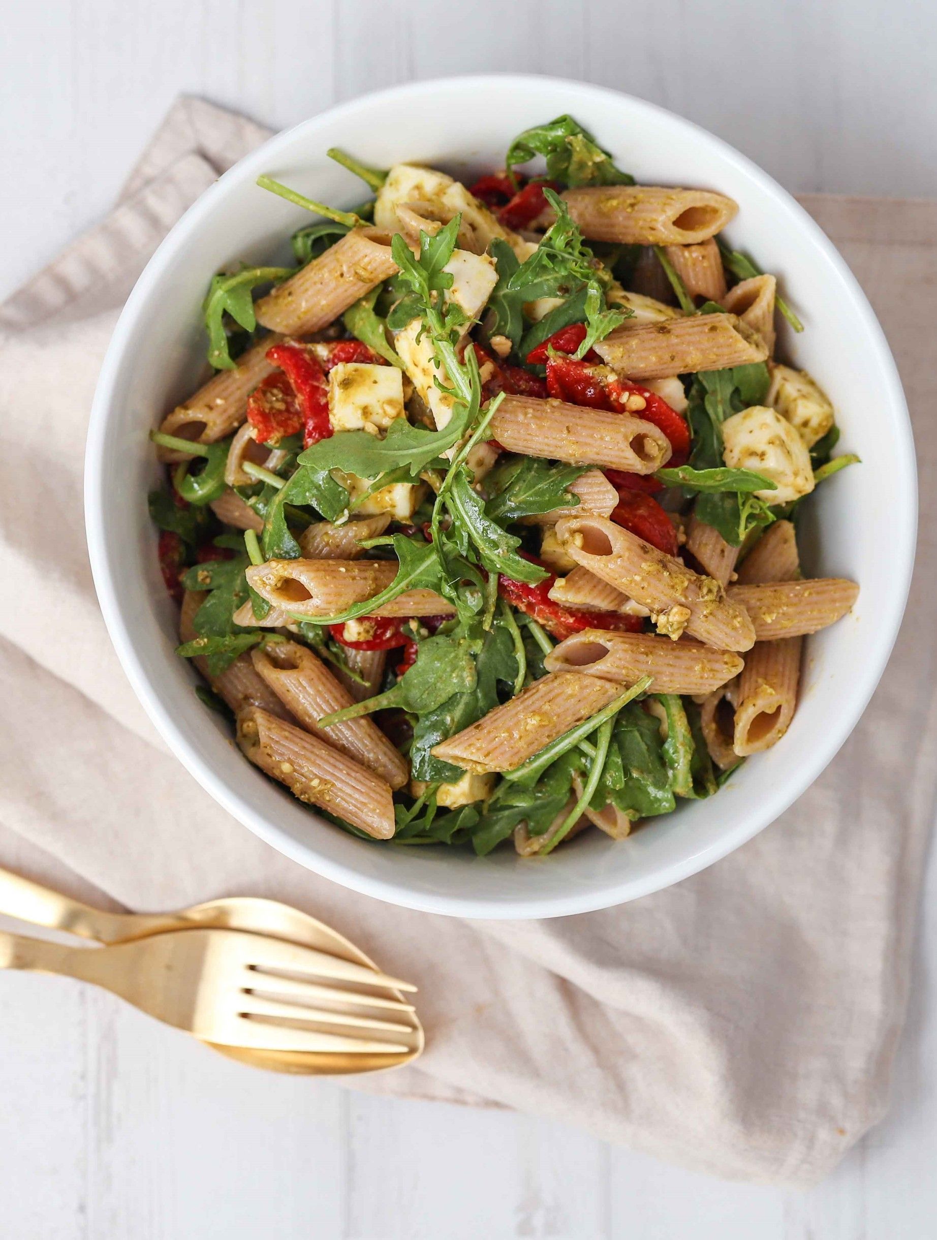 A bowl of pasta salad with vegetables and a fork on a table.