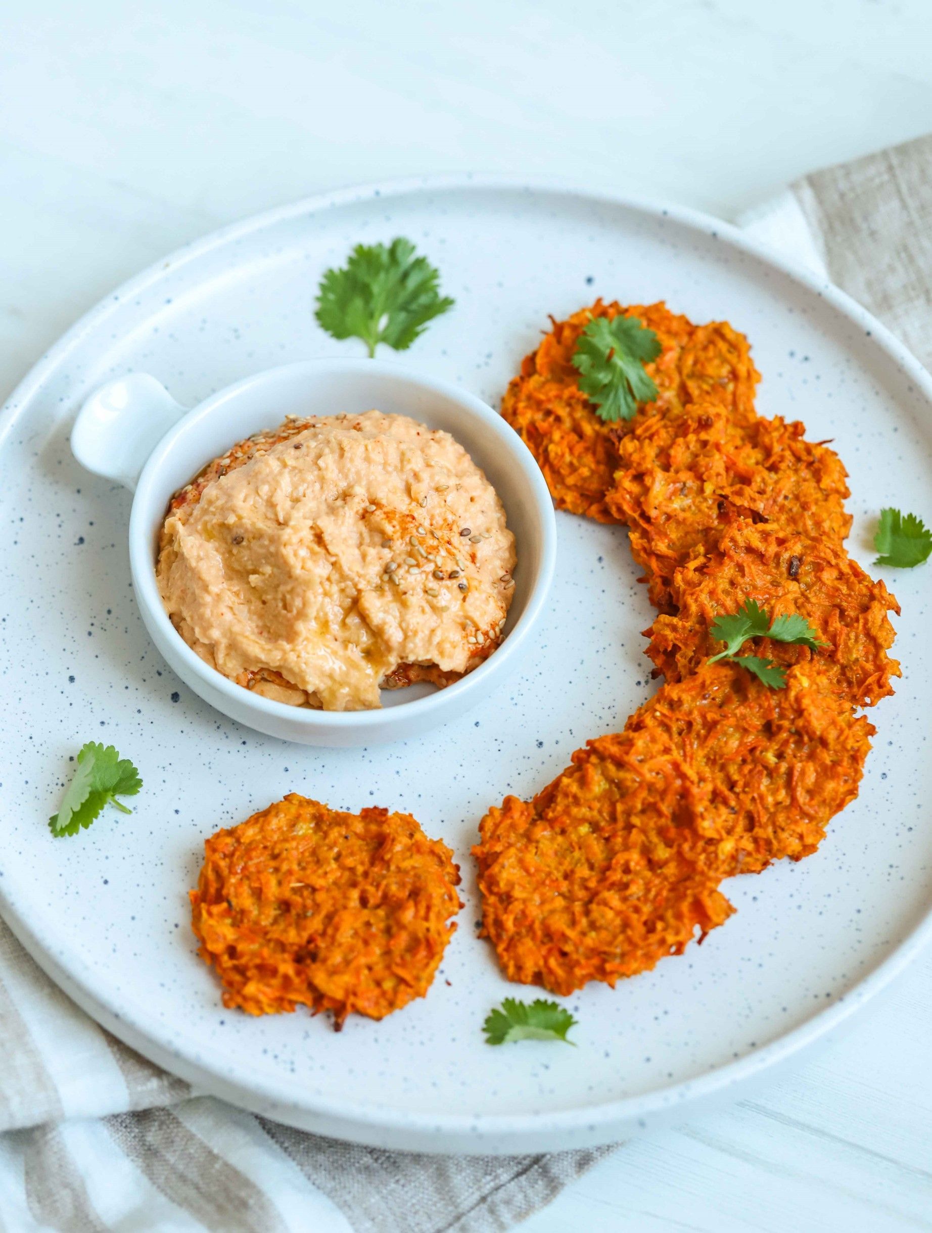 A white plate topped with carrot fritters and a bowl of dip.