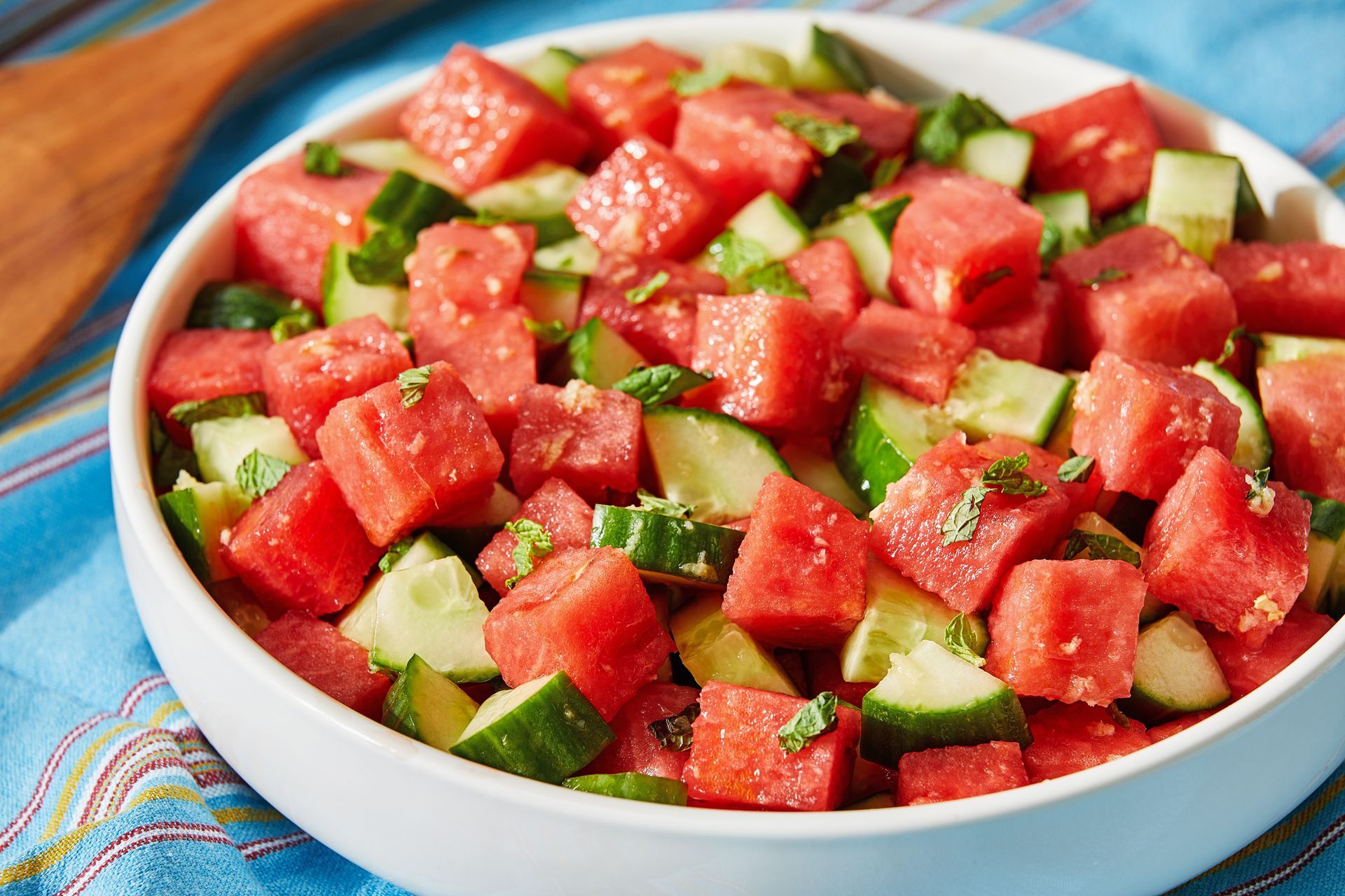 A bowl of watermelon and cucumber salad with a wooden spoon.