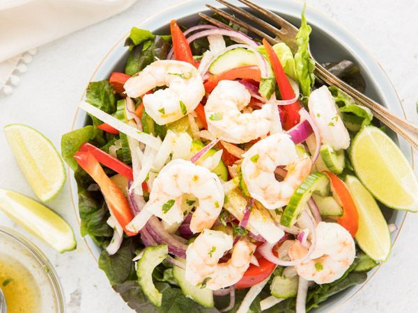 A bowl of shrimp salad with vegetables and a fork.