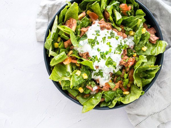A salad with lettuce , tomatoes , corn and ranch dressing in a bowl on a table.