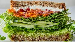 A close up of a sandwich with lettuce , carrots , cucumbers and avocado.