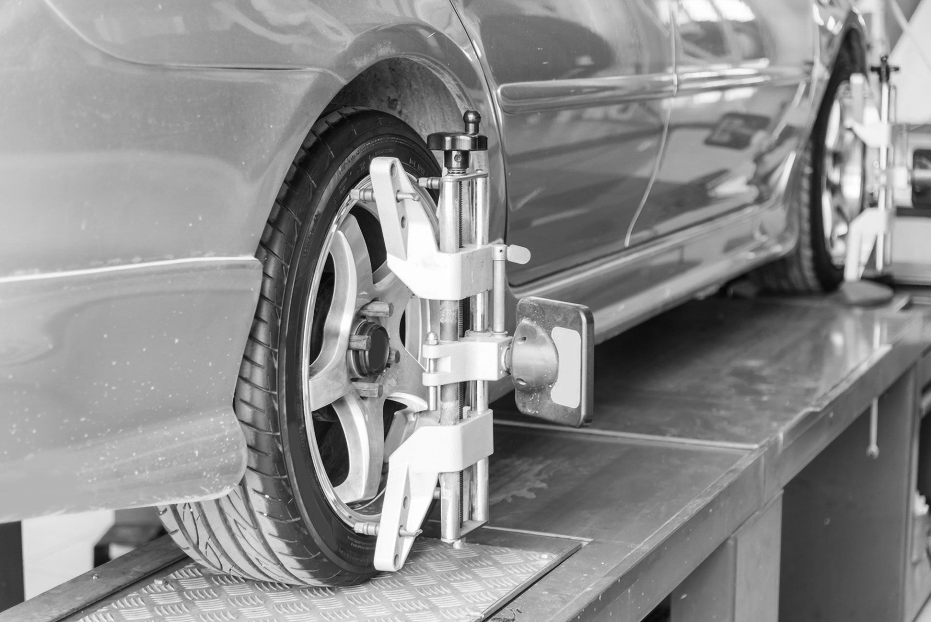 A silver car on a blue auto lift with wheel alignment sensors attached to the tires in a garage setting.