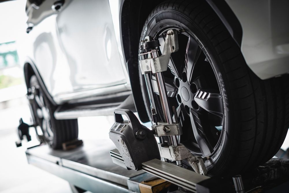 A white car undergoing wheel alignment, with specialized sensors attached to the wheels on a service lift.