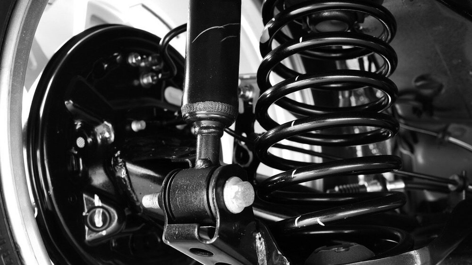 A black car shock absorber and coiled suspension spring mounted to a vehicle's undercarriage and brake assembly.