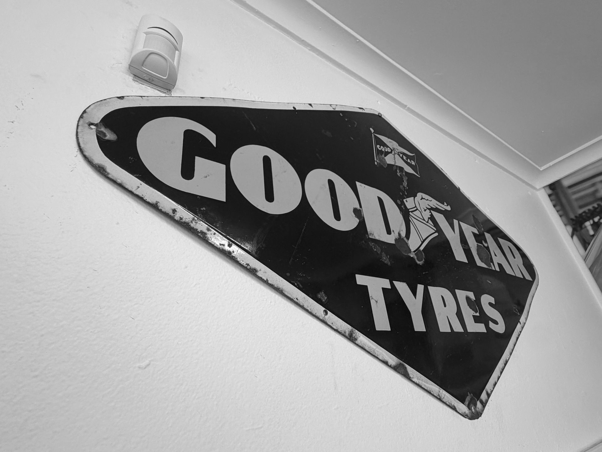 A vintage Goodyear Tyres sign with yellow text on a dark blue, shield-shaped background, mounted on a white wall.