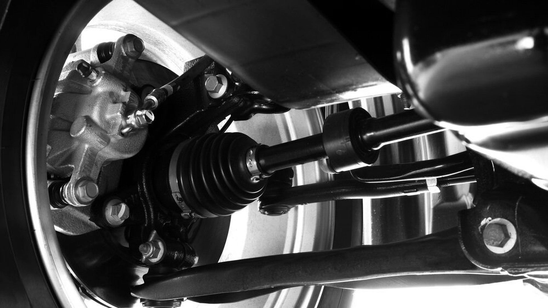 A close-up view of a car's wheel suspension, showing the axle, brake caliper, and control arm in a dark, metallic finish.