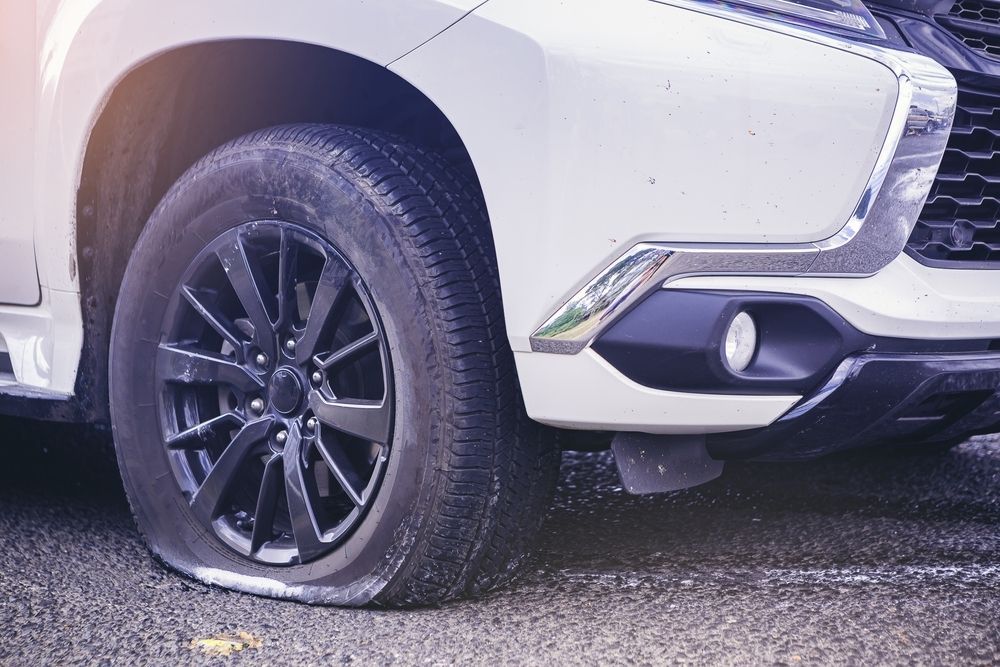 A white SUV parked on asphalt with a noticeably flat front tire.