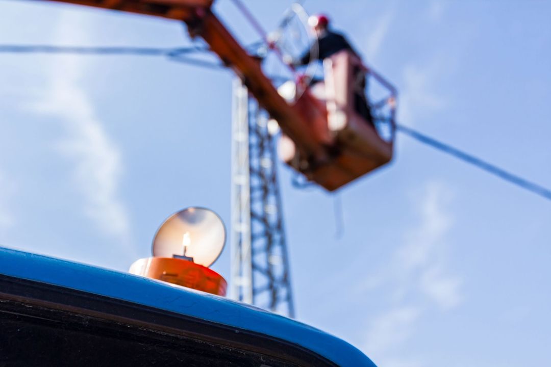Spia arancione accesa su un veicolo blu, operaio di un'azienda di servizi pubblici al lavoro su un camion con cestello sulle linee elettriche.