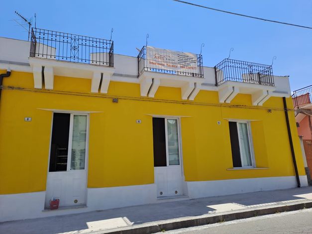 Edificio giallo con finiture e balconi bianchi. Finestre e porte fiancheggiano la facciata.